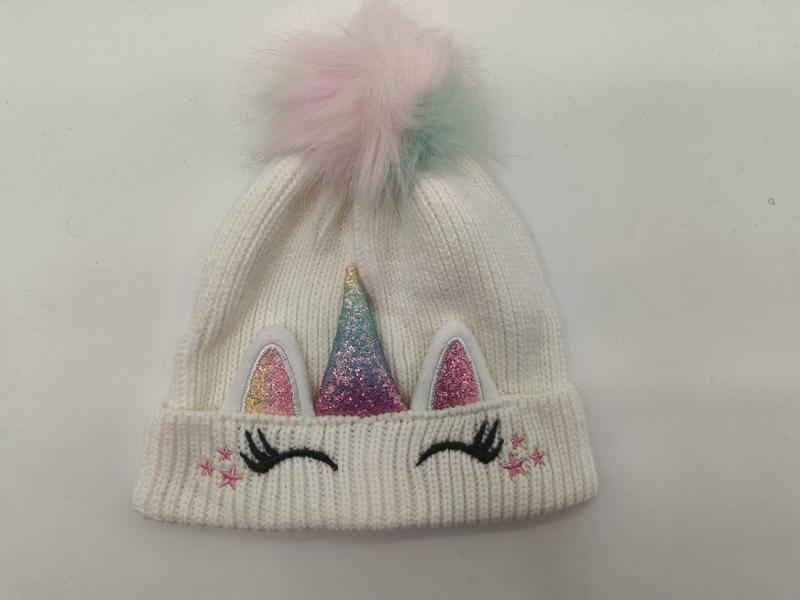 White ribbed knit children's unicorn beanie with glitter horn, pink ears, eyelashes, stars, and pastel rainbow faux fur pom-pom on top - wholesale price for USA buyers