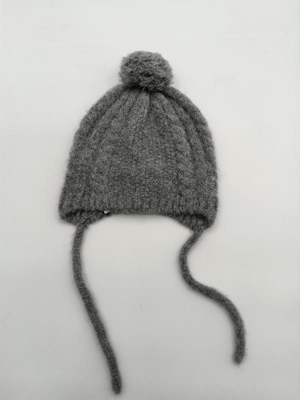 Gray cable knit baby winter hat with round pom pom on top and two long yarn tie strings on white background - contact for custom design quote