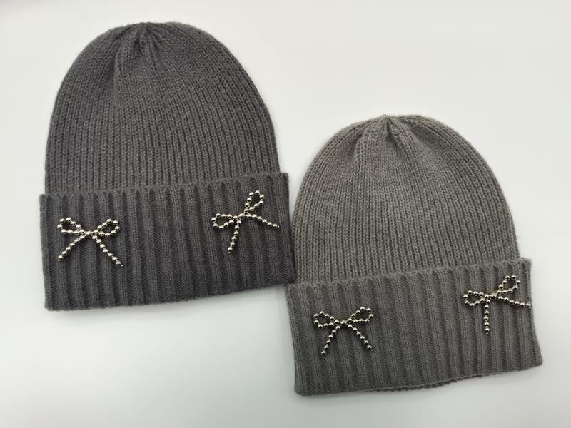 Two gray ribbed knit beanie hats with silver metal beaded bow embellishments on folded cuff, shown in dark and light gray - ask bulk pricing get discount