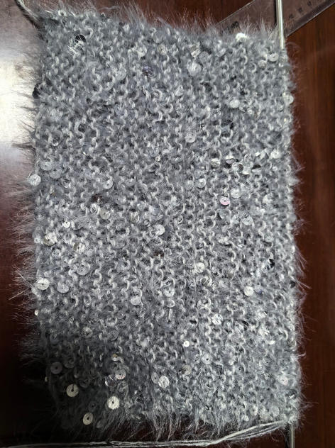 Close-up of grey fluffy knitted fabric swatch with scattered silver sequins on wooden surface - wholesale price for Middle East buyers