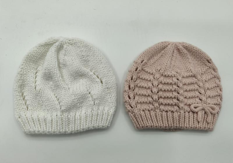 Two hand-knitted baby beanies side by side, white with leaf pattern and blush pink with horizontal texture and bow detail - factory direct price no middleman