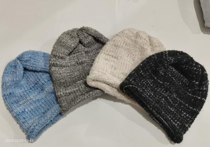 Four hand-knitted wool beanie hats in blue, gray, cream, and black laid flat on white surface - express production 15 days