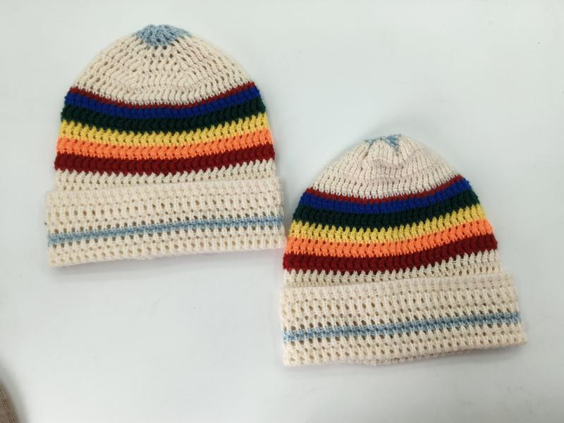 Two handmade cream crochet beanies with rainbow stripes in blue, green, yellow, orange, red on white background - winter accessories wholesaler
