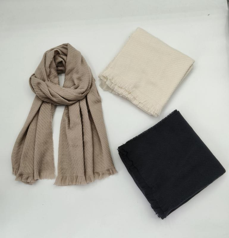 Three scarves displayed on white surface: draped taupe herringbone fringe scarf, folded cream scarf, and folded black scarf - sample order 10pcs available