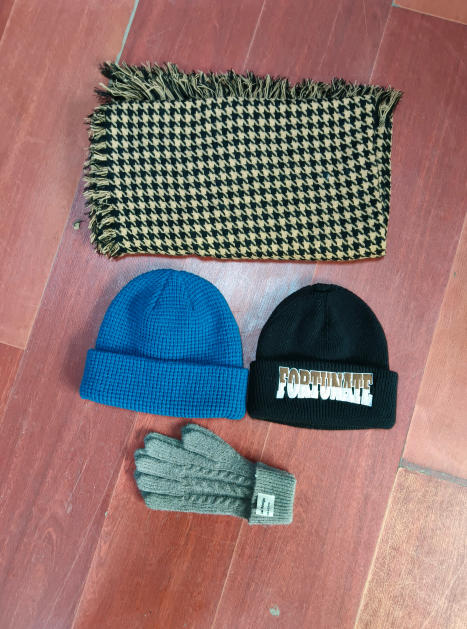Flat lay of tan black houndstooth fringe scarf, blue waffle knit beanie, black embroidered beanie, and gray cable knit gloves on wood floor - certified scarf manufacturer China - tiered pricing available ask quote