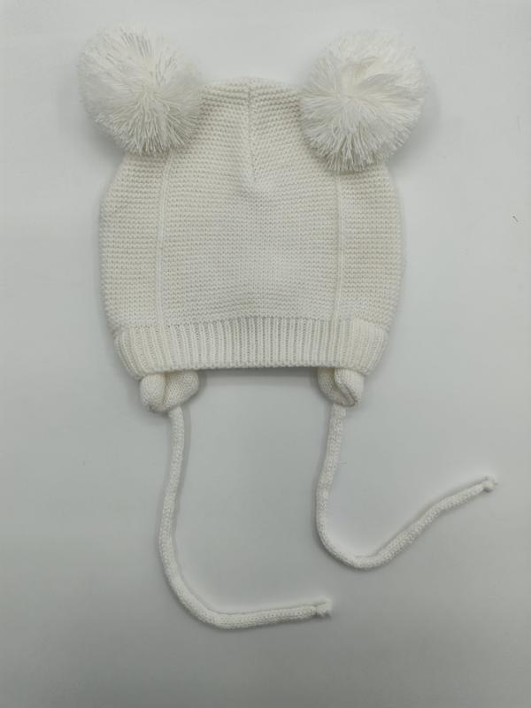 White knitted baby beanie with two fluffy pom poms on top and long chin tie strings, laid flat on white background - hotel amenity scarf supplier