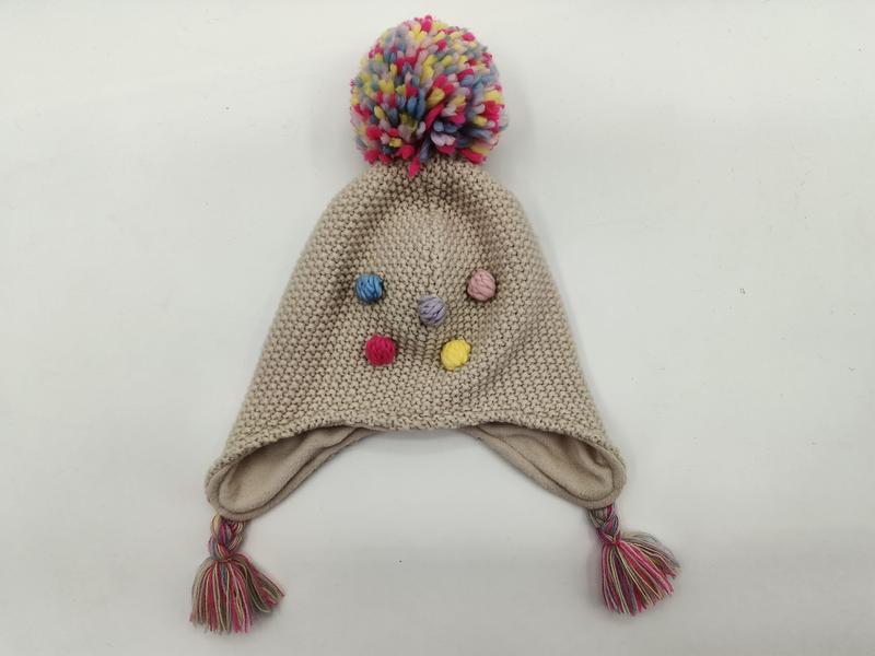Beige knitted children's earflap hat with large multicolor pom-pom on top, colorful bobble accents, and braided tassels - contact for custom design quote