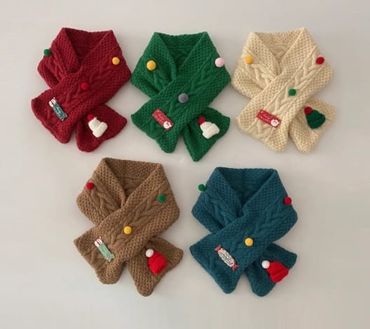 Five colorful children's cable knit crossover scarves in red, green, cream, brown, and teal with festive pom-pom and holiday charm decorations - wholesale price for Middle East buyers