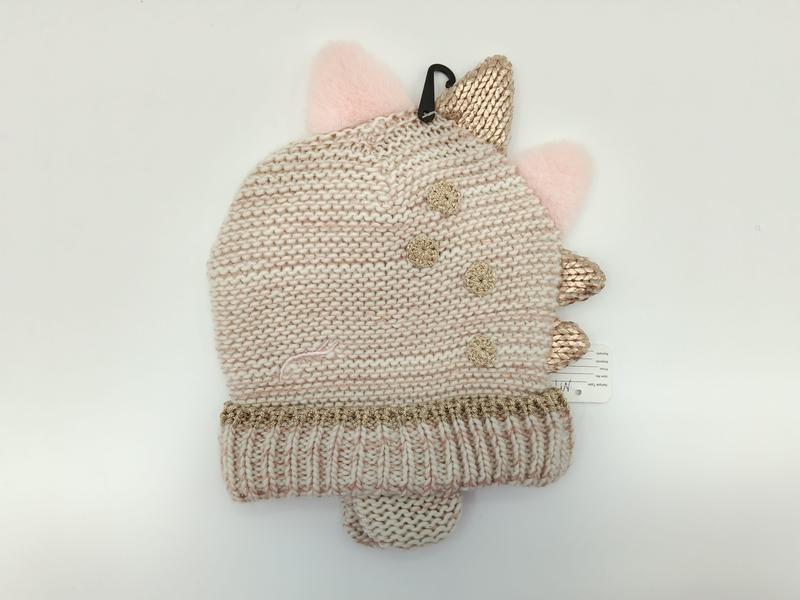 Children's cream knit dinosaur beanie hat with rose gold metallic spikes, pink pompom ears, and gold crochet flower accents on white background - wholesale price for Europe buyers