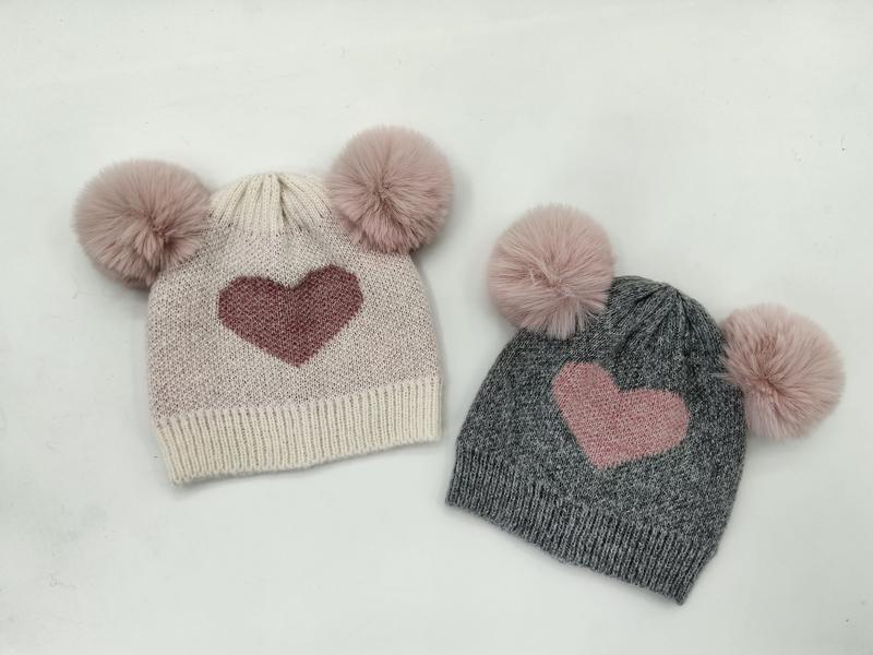 Two kids knit beanies with double faux fur pom poms and heart motif, one cream and one gray - no MOQ for stock designs