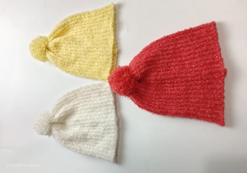 Three knitted pom-pom beanies in yellow, red, and white laid flat on white surface, fuzzy winter hats - wholesale price for Europe buyers
