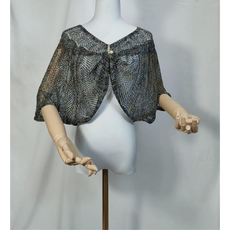 Blue gray metallic lace knit capelet shrug displayed on white mannequin with wooden hands, fastened with pearl brooch closure - contact for custom design quote