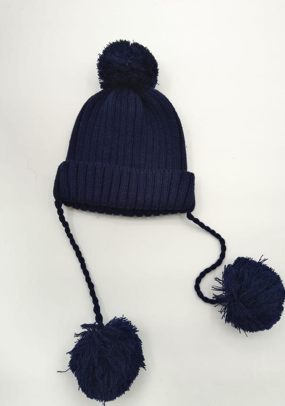 Navy blue ribbed knit winter beanie with top pom-pom and two long braided ties ending in large pom-poms - hotel amenity scarf supplier