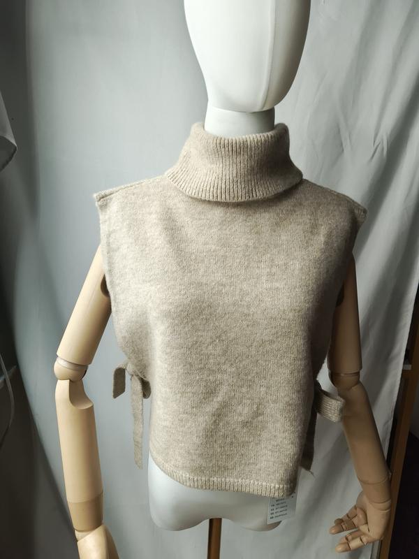 Beige sleeveless turtleneck knit sweater vest with side tie details displayed on a dress mannequin - EU REACH compliant material