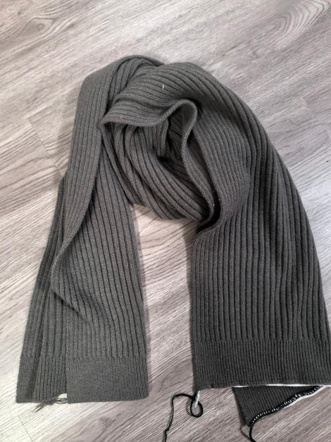 Olive green ribbed knit scarf laid flat on light wood floor, showing full length and texture - ask bulk pricing get discount
