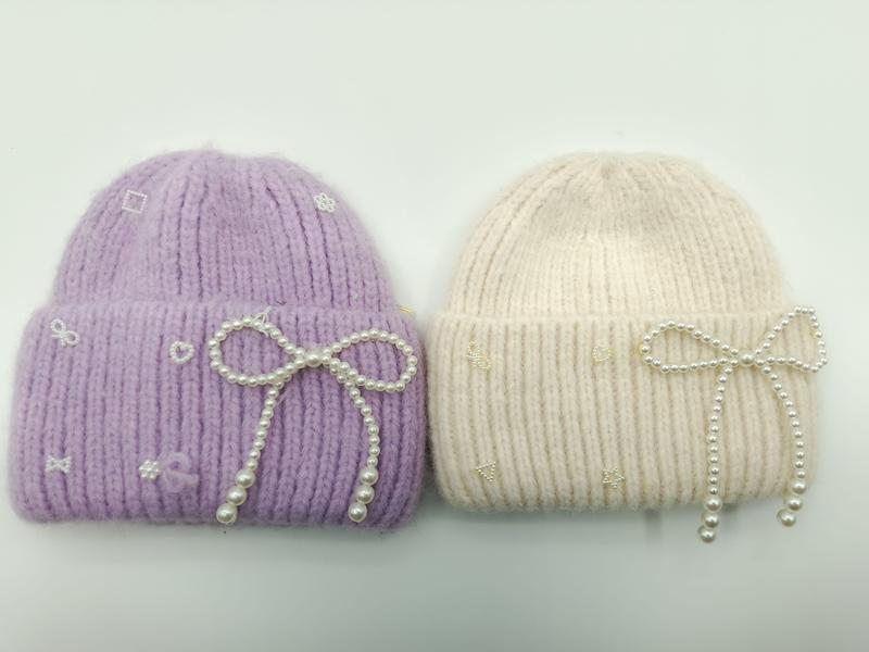 Two chunky knit beanies in lavender and cream with pearl bow decorations and embroidered motifs on white background - private label service available