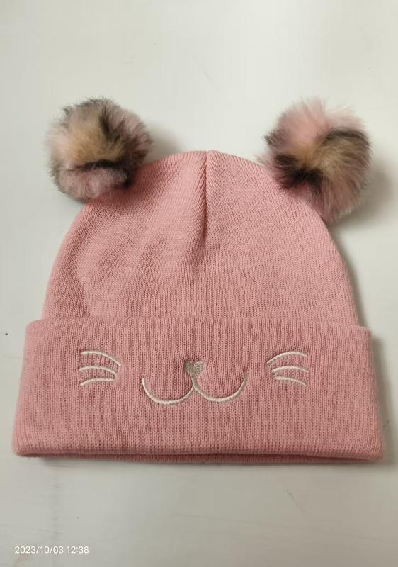 Pink knitted winter beanie hat with two faux fur pom poms and embroidered cat whiskers and nose on the cuff - email us get price list now