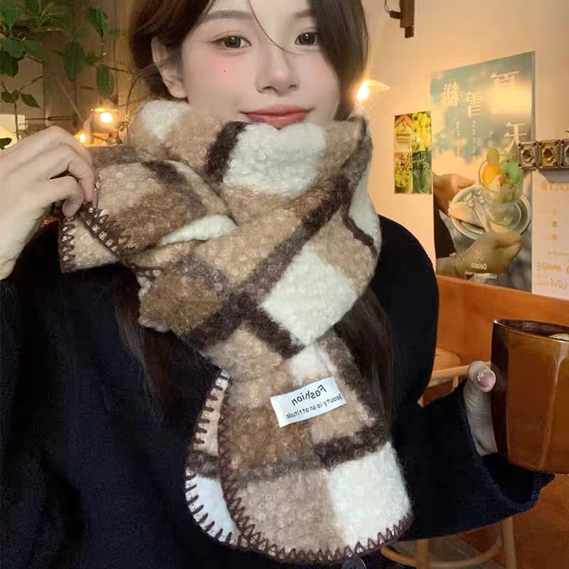 Young woman wearing a large plaid fuzzy beige and brown checked winter scarf with embroidered edges indoors - ISO 9001 quality controlled