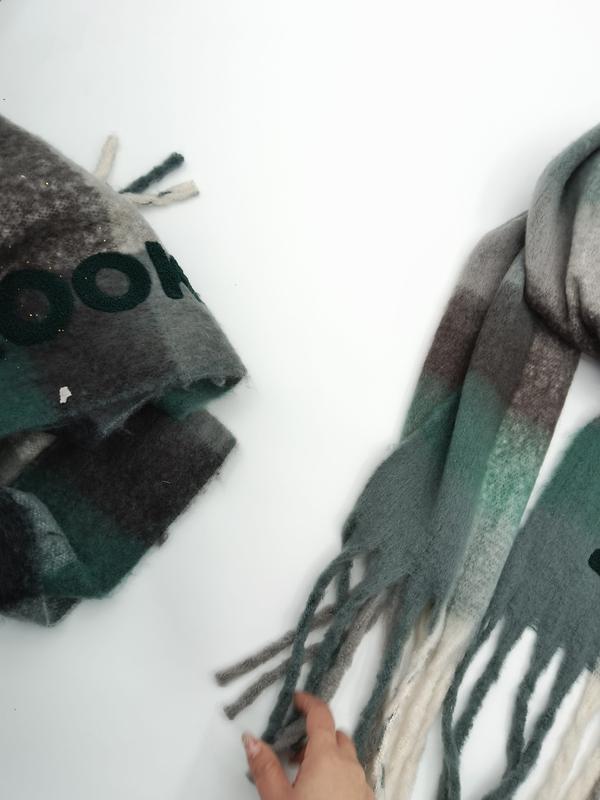 Two green grey and brown plaid wool blend scarves with fringed ends laid flat on white surface, one folded and one unfolded - corporate gift customization