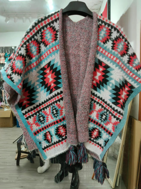 Open-front knitted poncho with Aztec geometric pattern in red, teal, black and white, with multicolor fringe tassels, displayed on hanger - gift shop wholesale supplier