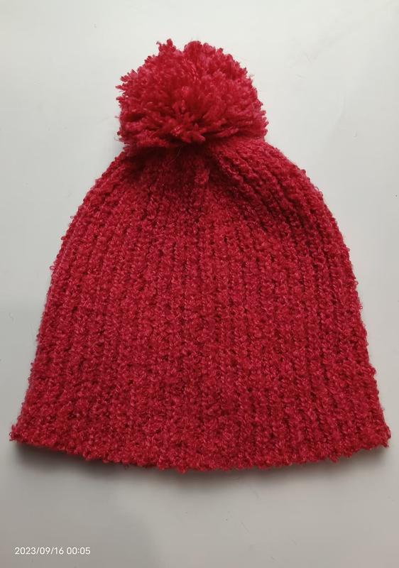 Red chunky ribbed knit winter beanie hat with large fluffy pom-pom on top, laid flat on white background - factory direct price no middleman