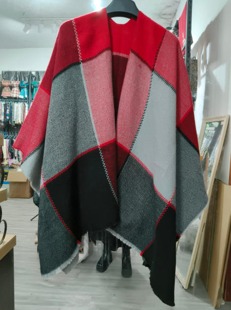 Oversized woven poncho cape with red, grey, and black geometric color block pattern displayed on hanger in store - free sample within 7 days