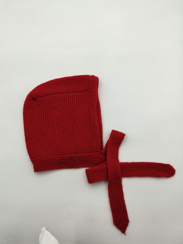 Red ribbed knit baby bonnet with chin tie strings laid flat on white background, handmade crochet infant cap - no MOQ for stock designs