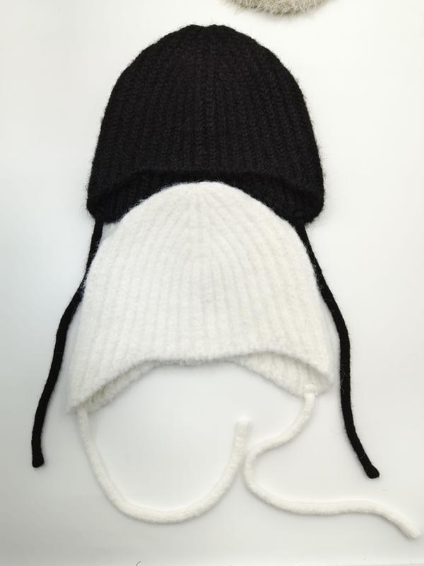 Two ribbed knit baby earflap hats with chin ties laid flat, one black and one white, on white background - ISO 9001 quality controlled