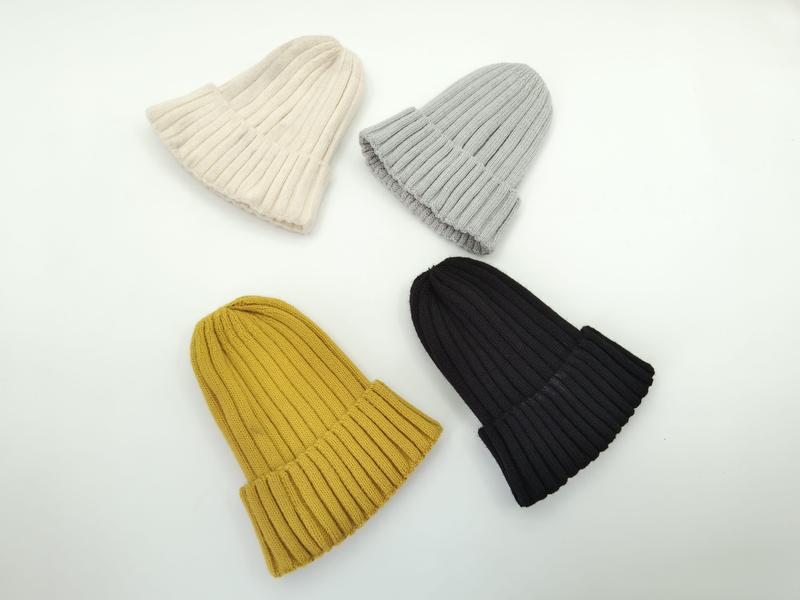 Four ribbed knit beanie hats laid flat in cream, light grey, mustard yellow, and black colorways on white background - bulk order 500+ pcs extra 8% off
