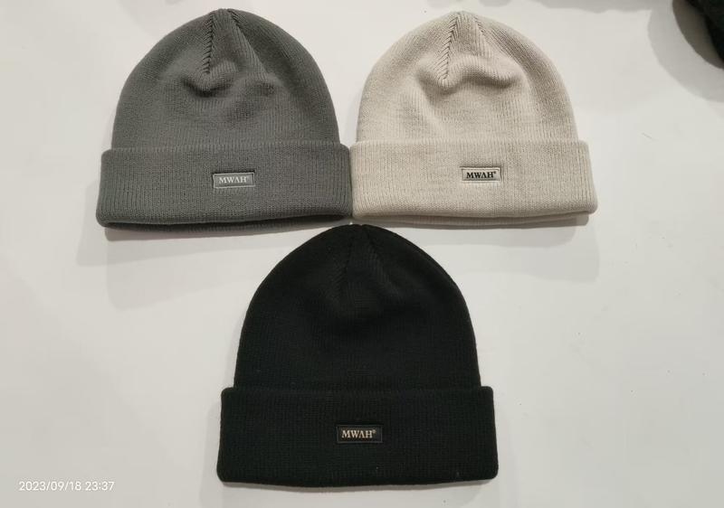 Three ribbed knit cuffed beanies in charcoal grey, cream beige, and black laid flat on white surface with logo patch - custom logo label accepted