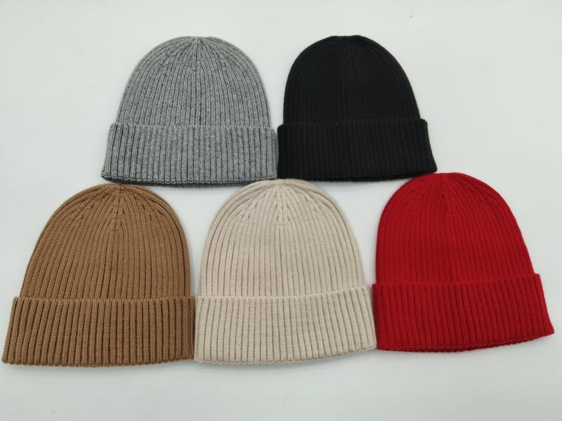 Five ribbed knit cuffed beanies in grey, black, camel, cream, and red arranged on white background - ISO 9001 quality controlled