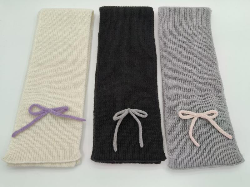 Three ribbed knit scarves in ivory, black, and grey, each with a small decorative yarn bow, laid flat on white background - certified scarf manufacturer China - boutique retail bulk order