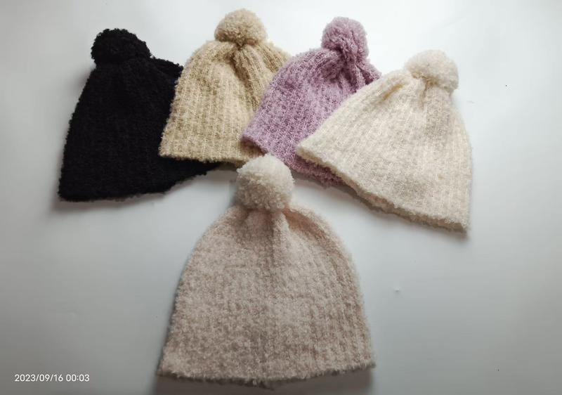 Five soft knitted pom-pom beanies in black, beige, lavender, cream and blush pink arranged on white surface - wholesale price for USA buyers