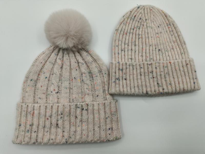 Two cream speckled knit winter beanies side by side, one with faux fur pom-pom and cable knit, one plain ribbed style - free sample within 7 days