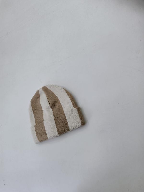 Small knitted beanie hat with wide tan and cream vertical stripes laid flat on white surface - free sample within 7 days