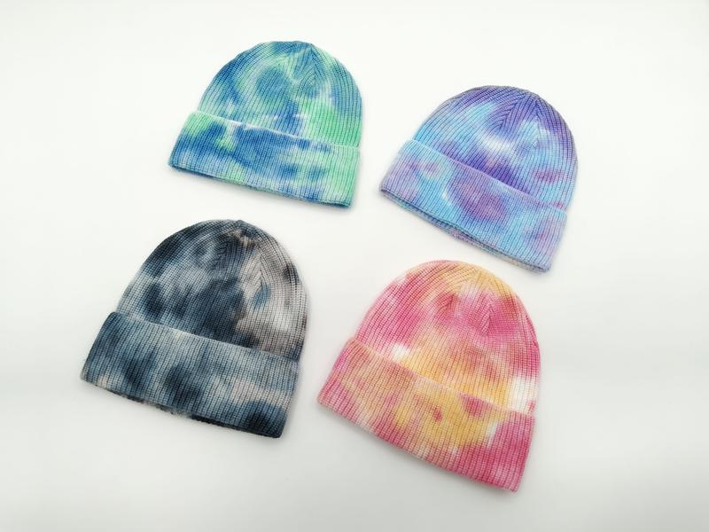 Four tie-dye ribbed knit beanies in blue-green, purple-blue, dark grey, and pink-yellow colorways on white background - hotel amenity scarf supplier