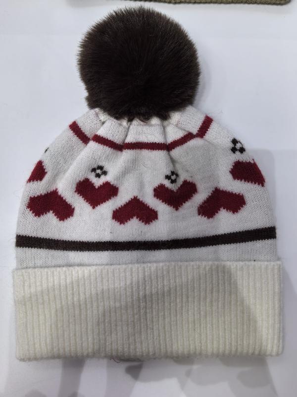 White knitted winter beanie hat with red heart pattern, dark brown faux fur pompom, and ribbed cuff on white background - BSCI audit passed supplier