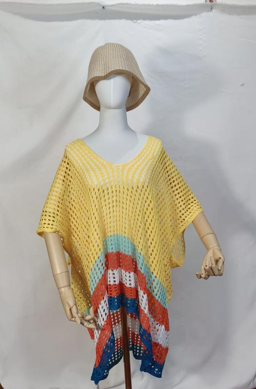 Mannequin wearing yellow crochet mesh poncho beach cover-up with multicolor stripes in teal, orange, white, blue at hem, paired with beige bucket hat - bulk order 20-day delivery